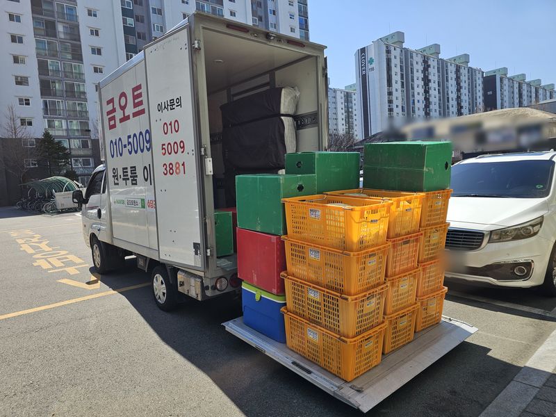 탑차 리프트 위에 노란 바구니와 초록 박스를 가득 올려 싣는 모습